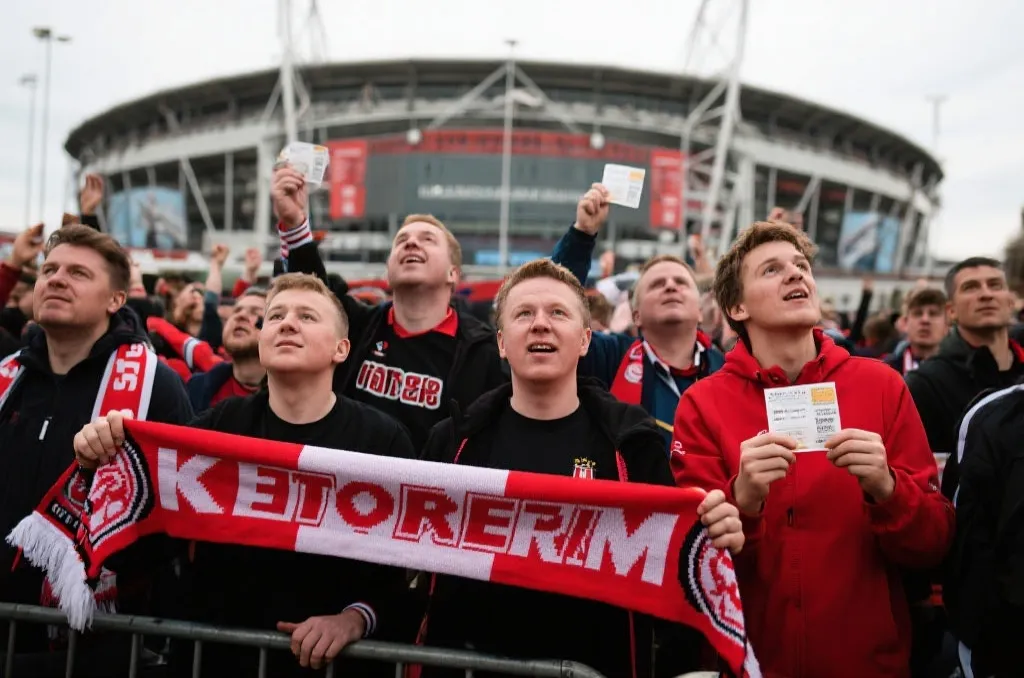 球迷在体育场外手持球票与围巾，期待比赛开场的热烈场景